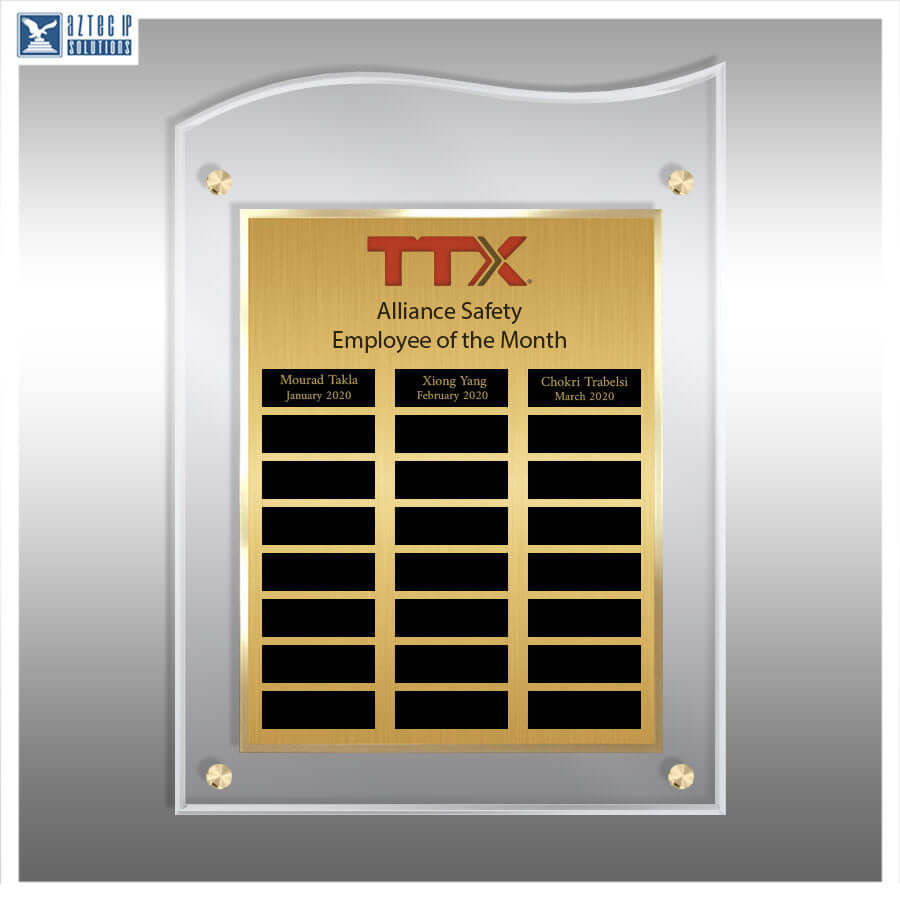 A square acrylic wall plaque with a brushed gold center panel and a silver border, mounted on a gray wall. The plaque features the red TTX logo and black nameplates for Employee of the Month awards, with three nameplates visible at the top and ten blank black rectangles below.
