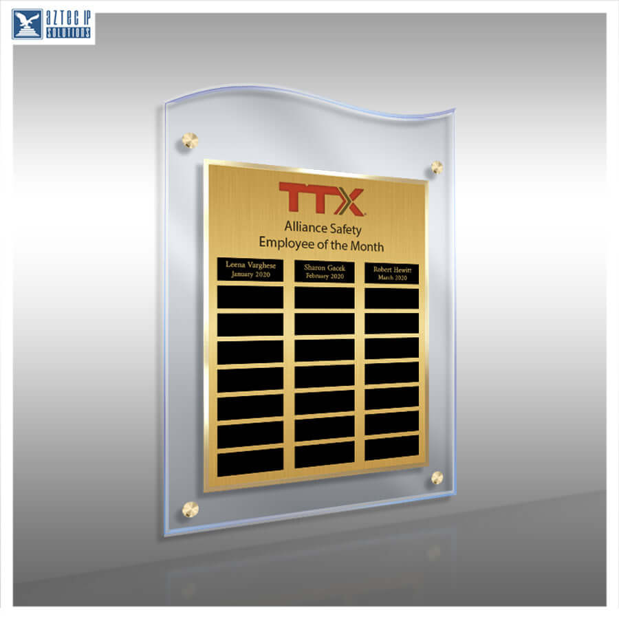 A wavy clear acrylic plaque with a gold-toned metal insert, mounted on a gray wall. The insert features the red and black TTX logo and text for 'Employee of the Month' with three black nameplates at the bottom.