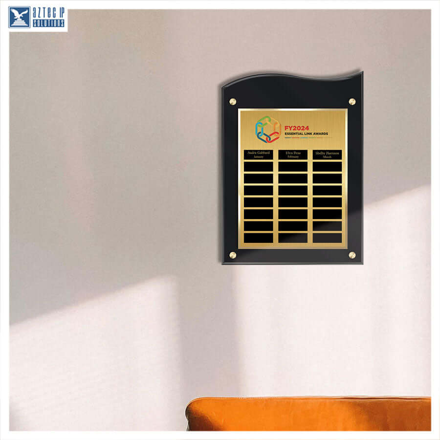 A black acrylic wall plaque with a gold metal plate, featuring multiple black name slots and a colorful logo at the top, mounted on a beige wall.