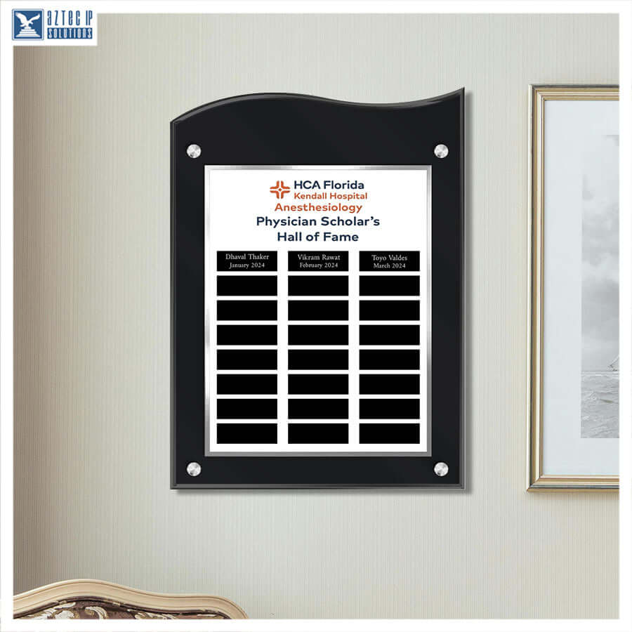 A black acrylic wall plaque with a white insert, mounted on a beige wall. The plaque features the text 'HCA Florida Kendall Hospital Anesthesiology Physician Scholar's Hall of Fame' and multiple black nameplates for physicians.