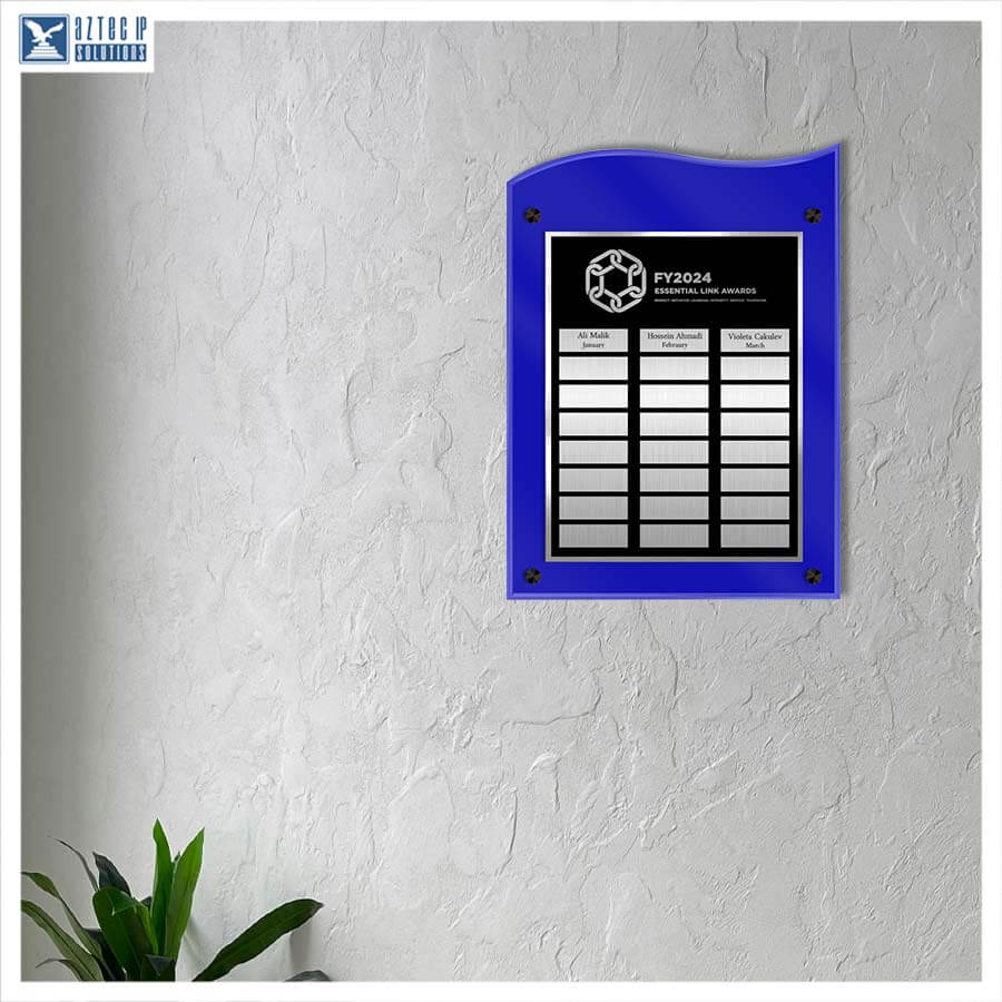 A blue acrylic wall plaque with a black center panel displaying event details for FY2024, mounted on a textured white wall next to a small green plant.