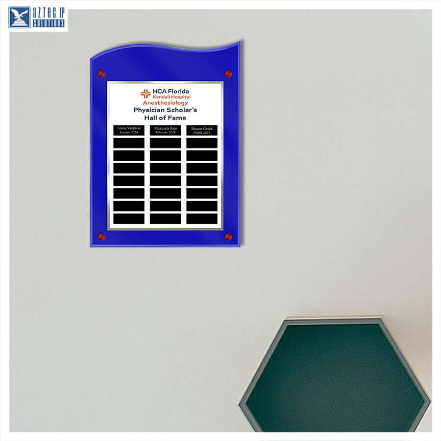 A blue acrylic wall plaque with a white insert displaying the HCA Florida Hospital Physician Scholar's Hall of Fame, mounted on a light gray wall. A second hexagonal green-framed sign is partially visible in the lower right corner.