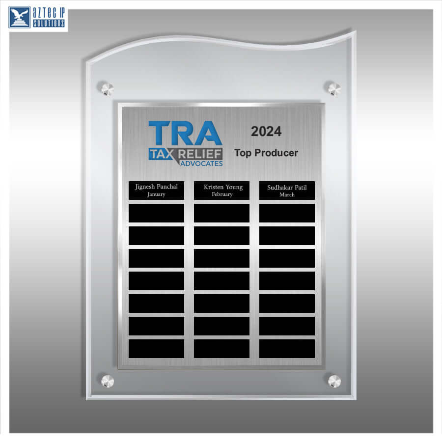 A silver acrylic wall plaque with a brushed metal center panel, shown on a gray gradient background. The plaque features the 'TRA Tax Relief Advocates 2024 Top Producer' logo at the top, with three black nameplates and twelve additional blank black nameplates arranged in a grid below.
