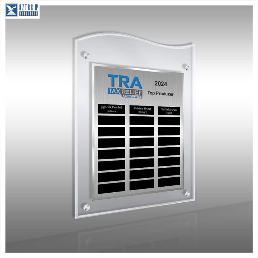 A silver acrylic wall plaque with a wavy top border, featuring a brushed metal insert that reads 'TRA TAX RELIEF HONORABLES 2024 Top Producer' with black nameplates below, shown on a gray gradient background.
