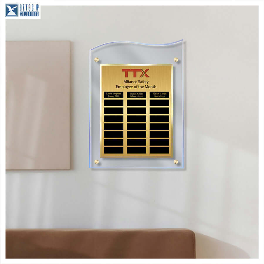 A gold and black acrylic 'Employee of the Month' wall plaque mounted on a white wall, featuring the red 'TTX' logo and black nameplates below.